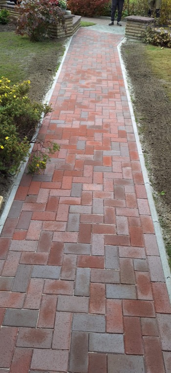 Gepflasterter Gartenweg mit roten und grauen Steinen und hellen Einfassungen